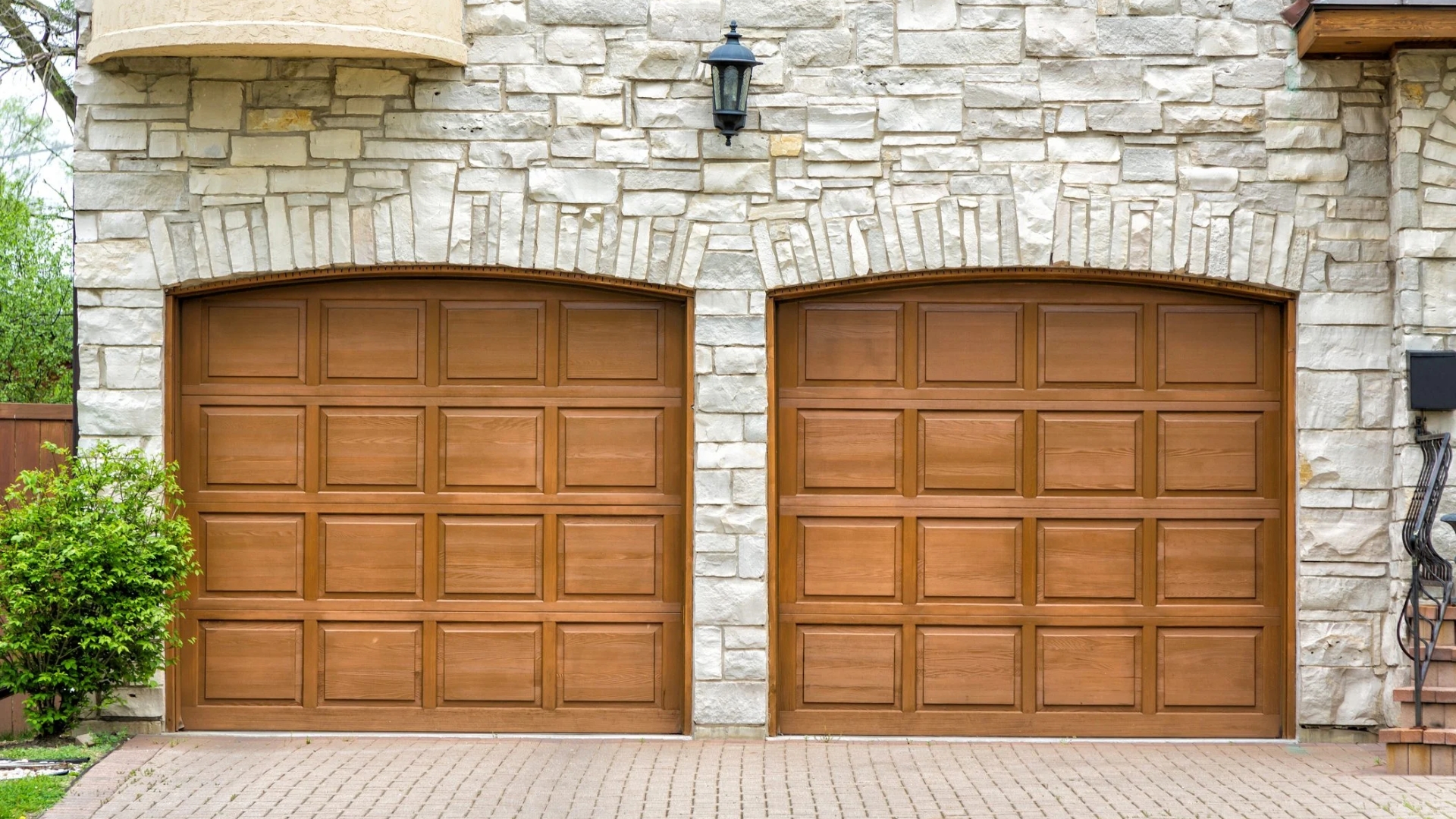 Wooden garage doors with a classic finish on a stone house exterior.